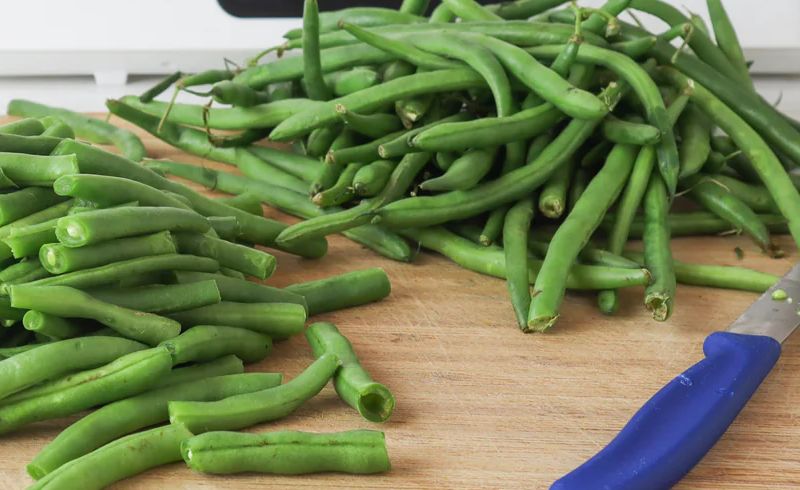 A blue knife and newly-sliced green beans for dehydration.
