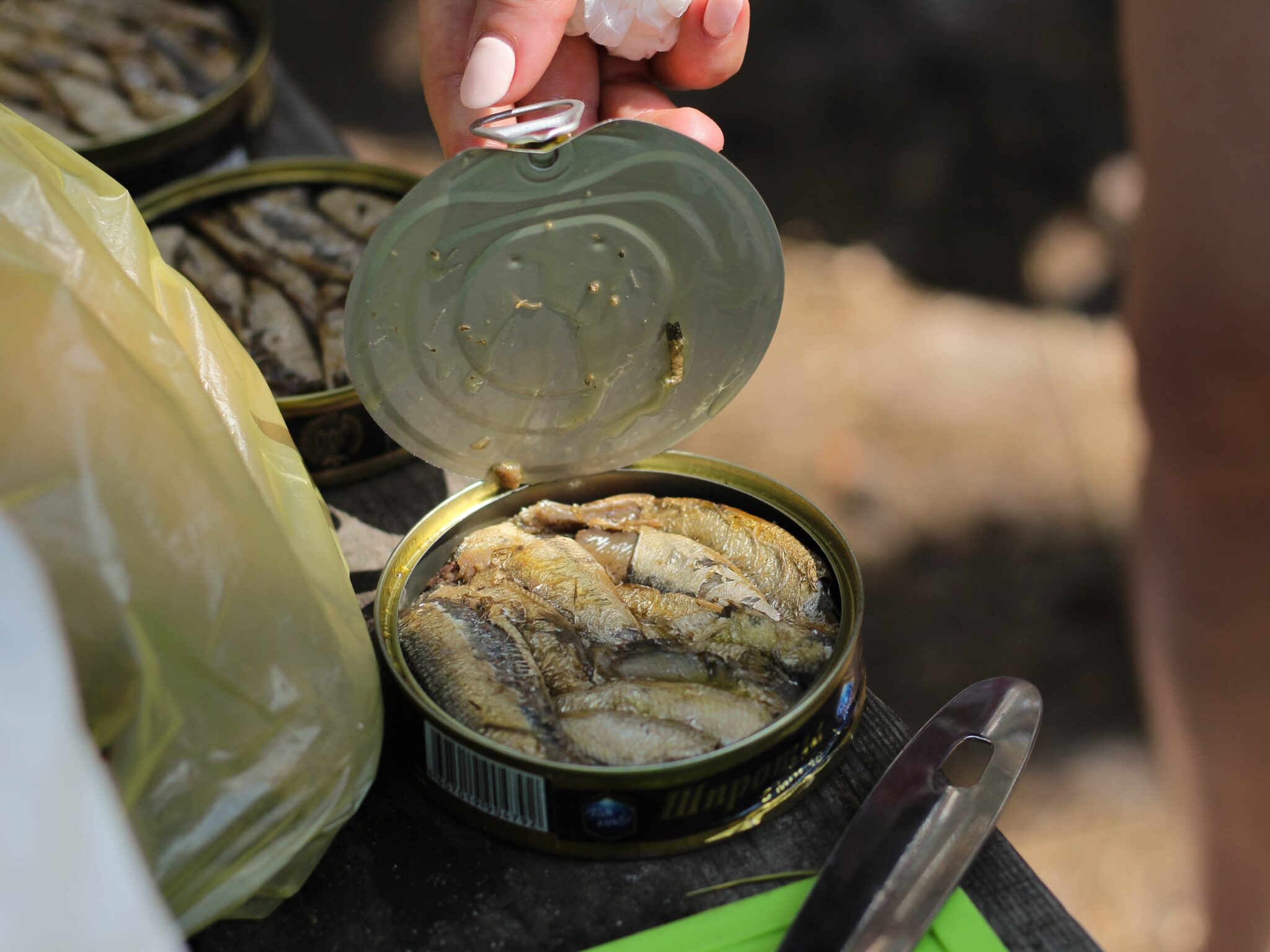cheap foods that last a long time A hand opening a new can of tuna fish beside other opened tuna cans.