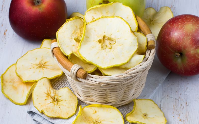 The best foods to dehydrate for long-term storage Dehydrated sliced apples inside the tray basket and two red apples outside it.