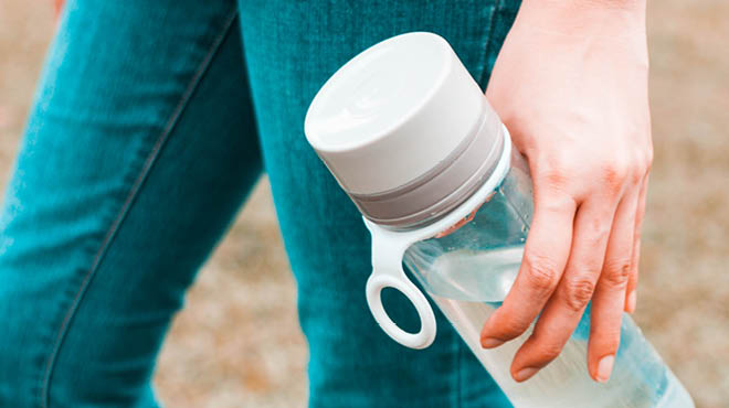 A girl holding a plastic bottle full of tap water outdoors. 