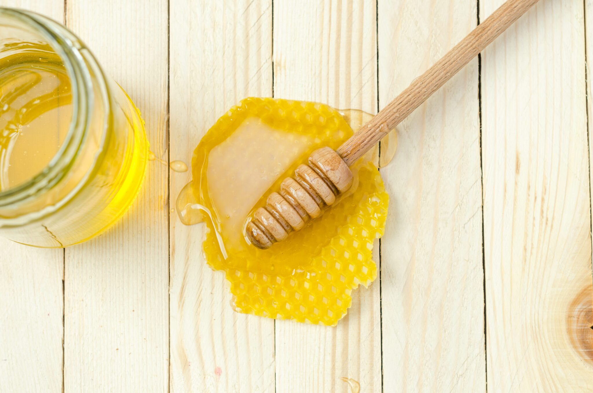 cheap food that last a long time A glass of honey and some honey spillage beside the honey dipper on the wood table.