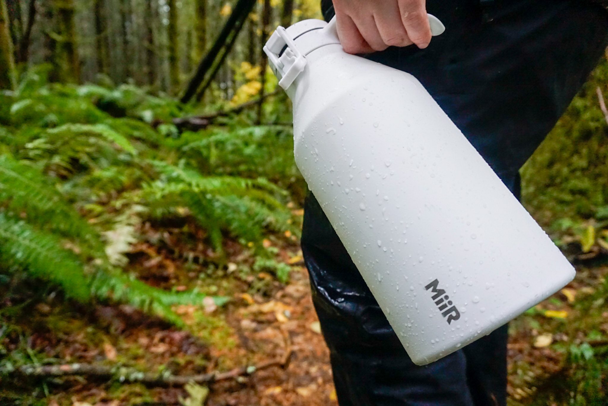 A man holding a durable, white water jug in the forest. 