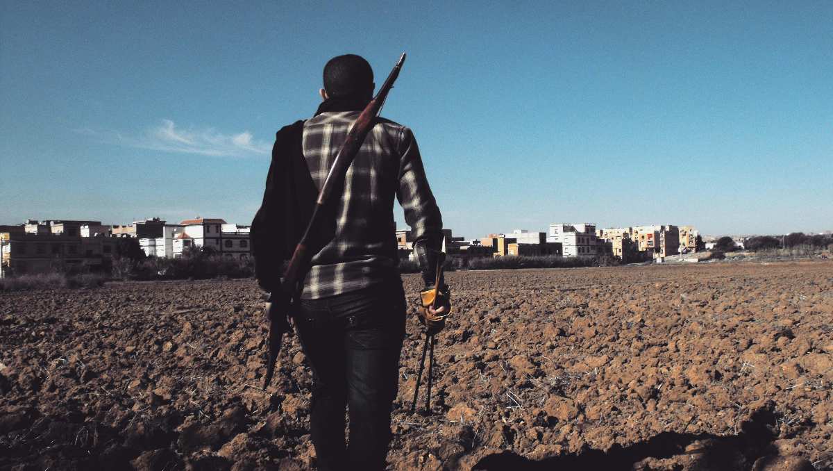 A man walking with survival weapons on a vacant land.